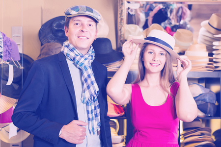 smiling young wife and husband choosing dress hats in the storeの写真素材