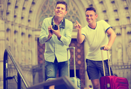 Smiling  male couple standing with baggage at street and taking photos 
の写真素材