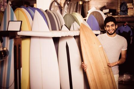 Portrait of happy cheerful positive  man with board for surfing in the shopの写真素材