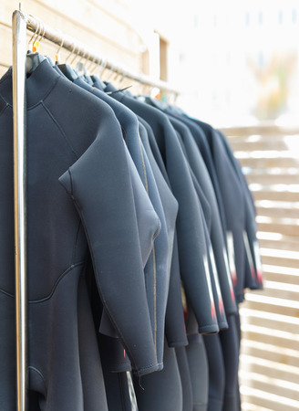 Black fashionable modern  surfing wetsuits hanging on rack for rent in surf clubの写真素材