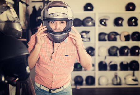 Happy young male customer is trying up modern helmet in the sport store.の写真素材