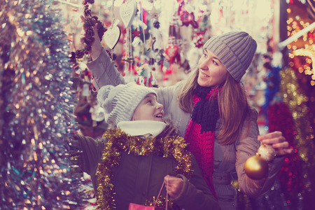 Young girl and her mother are choosing Christmas decorations in the market outdoor.の写真素材