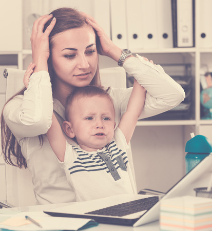 Perplexed female with kid is having issue while working behind laptop in office.の写真素材