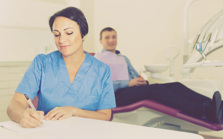 worker dentist professional sitting in medical room with adult patientの写真素材