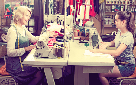Two attractive women sewing with professional equipment at atelierの写真素材