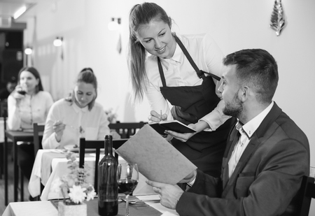 Welcoming female waiter is taking order from businessman in restaurante indoor.の写真素材