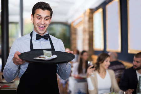 Professional waiter man holding serving tray in restaurant with tipsの写真素材