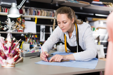 Smiling woman tailor working with marker for modeling clothes at atelierの写真素材
