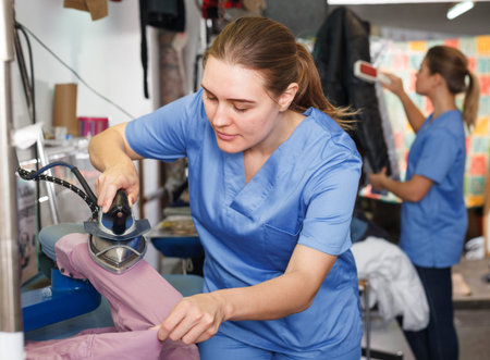 Young woman working in modern dry cleaning salon, ironing clothes on professional equipmentの写真素材