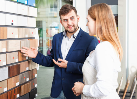 Competent diligent positive  seller in showroom helping young satisfied smiling female client to choose furniture materials for her apartmentの写真素材