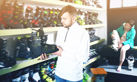 Ordinary sporty guy looking for modern ski boots in sport goods storeの写真素材
