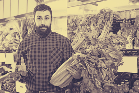 Young male seller offering celery in grocery shopの写真素材