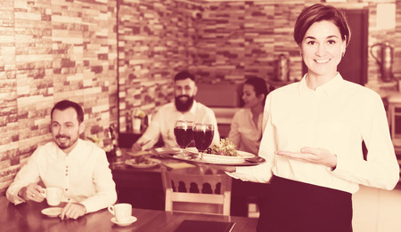 Young female waiter bringing order for guest in country restaurantの写真素材