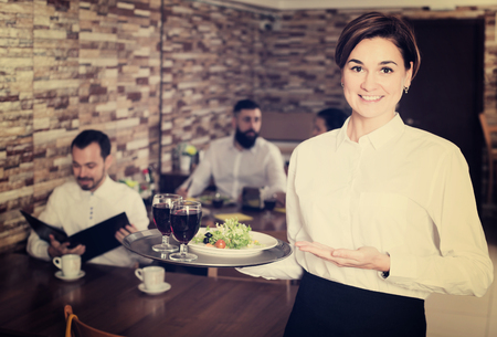 Young woman waiter demonstrating country restaurant to visitorsの写真素材