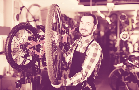 positive man in apron considering composition of wheel for bicycleの写真素材