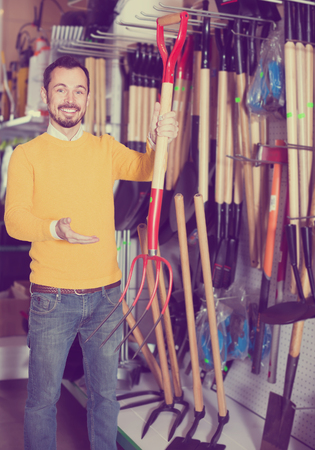 Smiling guy deciding on best hayfork from assortment in garden equipment shopの写真素材