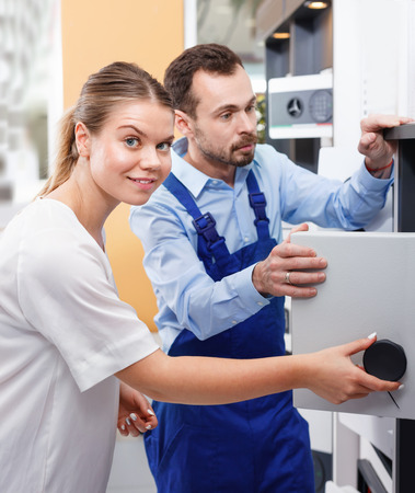 Attractive smiling glad  girl consulting about purchase of home safe with worker in specialty workshopの写真素材