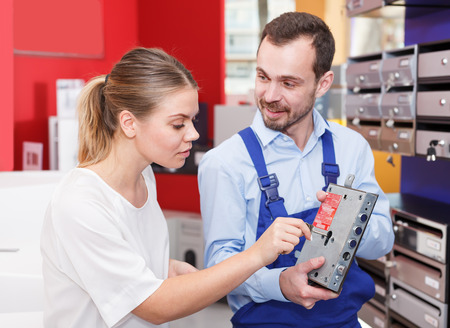 Man in blue overalls showing door lock to nice female client in hardware storeの写真素材