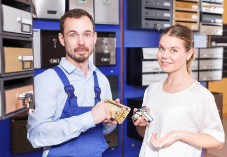 Competent seller consulting young woman about purchase of door lock in specialty workshop