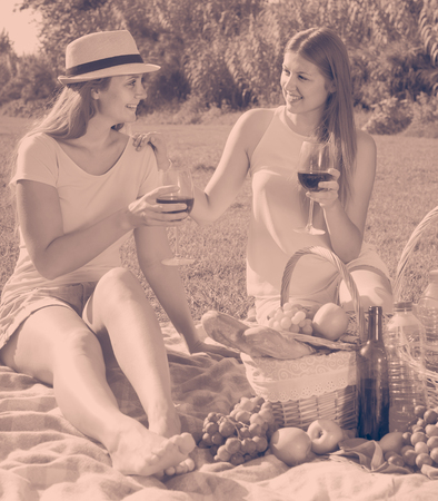 Two smiling american young women enjoying wine and conversation on picnic outdoorsの写真素材