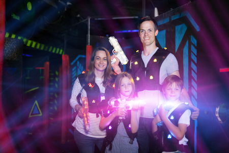 Modern young parents and children playing laser tag in dark labyrinth in bright beams of laser pistolsの写真素材