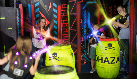 Group of happy kids and adults having fun on dark lasertag arena in colorful beams of laser gunsの写真素材