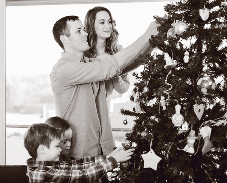 Parents and children putting decorations on Christmas tree at homeの写真素材