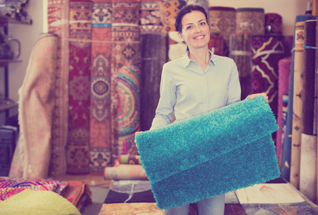Smiling female keep in hand colored carpet in interior shopの写真素材
