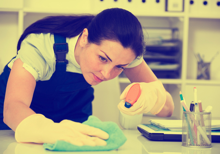 Portrait of adult female cleaning office table with rag and cleanserの写真素材