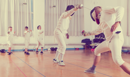 Adults and teens wearing the fencing uniform practicing with foil in a gymの写真素材