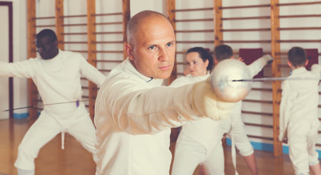 Portrait of focused man wearing fencing uniform practicing with foil in gymの写真素材