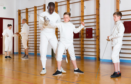 Fencing instructor explaining to young fencers an effective movements and techniques in training roomの写真素材
