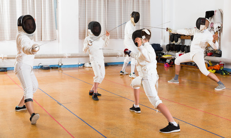 Adults and teens wearing fencing uniform practicing with foil in the gymの写真素材