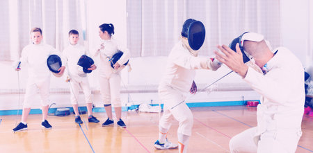 Diligent positive cheerful smiling coaches demonstrating to young athletes attack movements with...