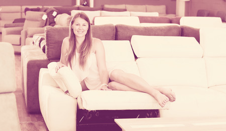 Portrait of positive woman buyer sitting barefoot on the sofa in furniture shopの写真素材