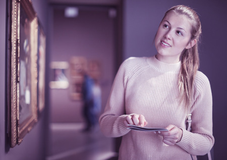 Portrait of young woman with guide looking at pictures in a museum of artsの写真素材