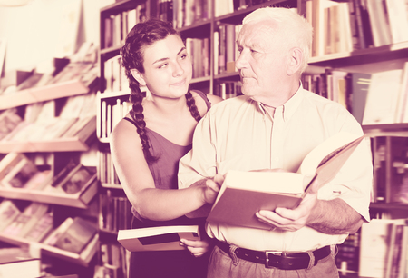 Old man with laughing girl are reading books in bookstoreの写真素材