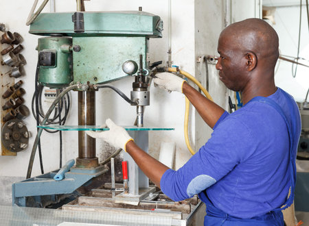Adult African American craftsman working on glass drilling machine table in workshop