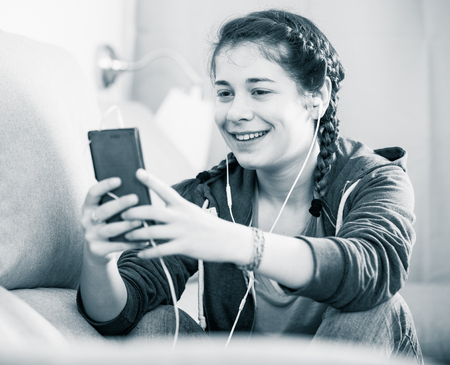 Smiling girl texting with her phone and listening to music at homeの写真素材