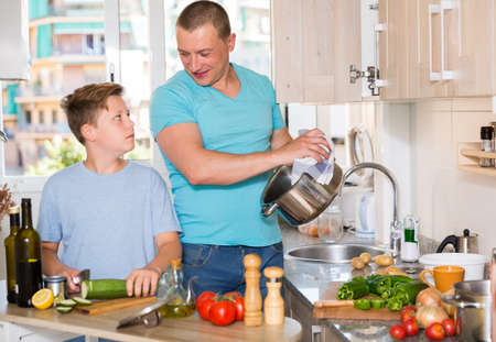 Boy and his father are cooking soup together in the kitchen at home.の写真素材