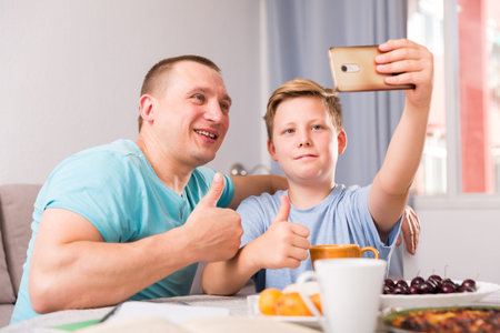 Guy with his father are resting and taking selfie by phone at the home.