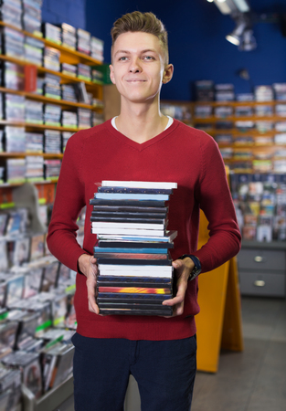 Positive adult guy holding pile of boxes with DVDs bought in shopの写真素材