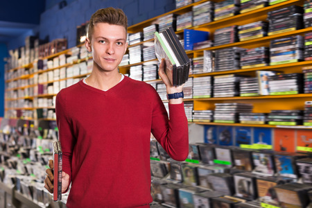 Positive man looking for interesting movies on shelves of CD shopの写真素材