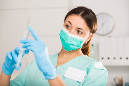 Young female nurse in mask holding syringe for injection in hospitalの写真素材