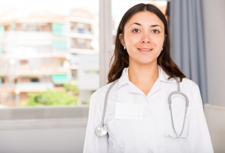 Portrait of young  woman doctor in white uniform standing in clinic's officeの写真素材