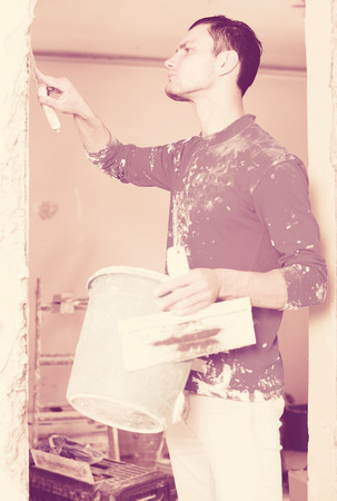 Construction worker wearing casual clothing with wall plastering tools renovating apartment houseの写真素材