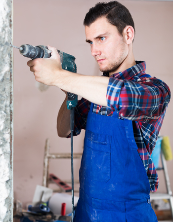 serious professional builder drilling hole in wall with perforator in a repairable roomの写真素材