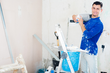 Smiling young man engaging in repair of his house and holding bag of puttyの写真素材