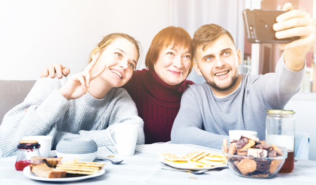 Young happy couple making selfie with smiling senior woman at homeの写真素材