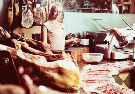 portrait of young smiling woman 30s buying dried ham in delicatessen shopの写真素材